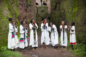 Siete jóvenes etíopes vestidas con su atuendo tradicional cantan juntas frente a una de las once iglesias monolíticas ubicadas bajo el nivel de la tierra.